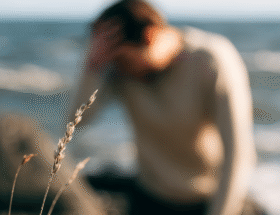 En man som sitter på en klippa på stranden. Yr. Bilden är suddig.