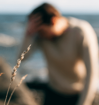 En man som sitter på en klippa på stranden. Yr. Bilden är suddig.